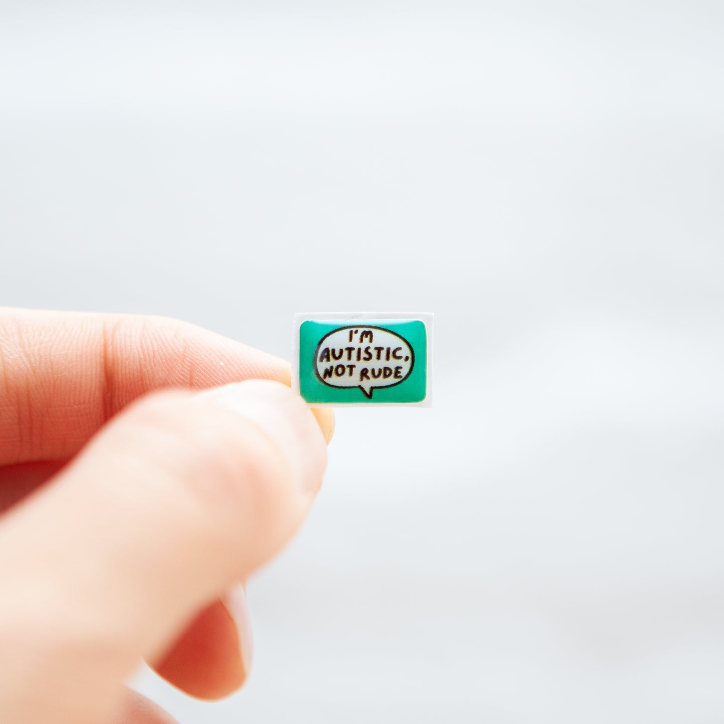 An 'I'm Autistic Not Rude' sticker with a bright turquoise background, designed for name badges and ID tags. Ideal as an autistic sticker for name badges and ID tags.