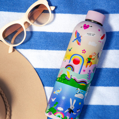 Badgie Be Yourself Steel Water Bottle BPAFree. Product image of the steel bottle at the beach, on a towel, used for travel and adventure, with sunglasses and hat visible