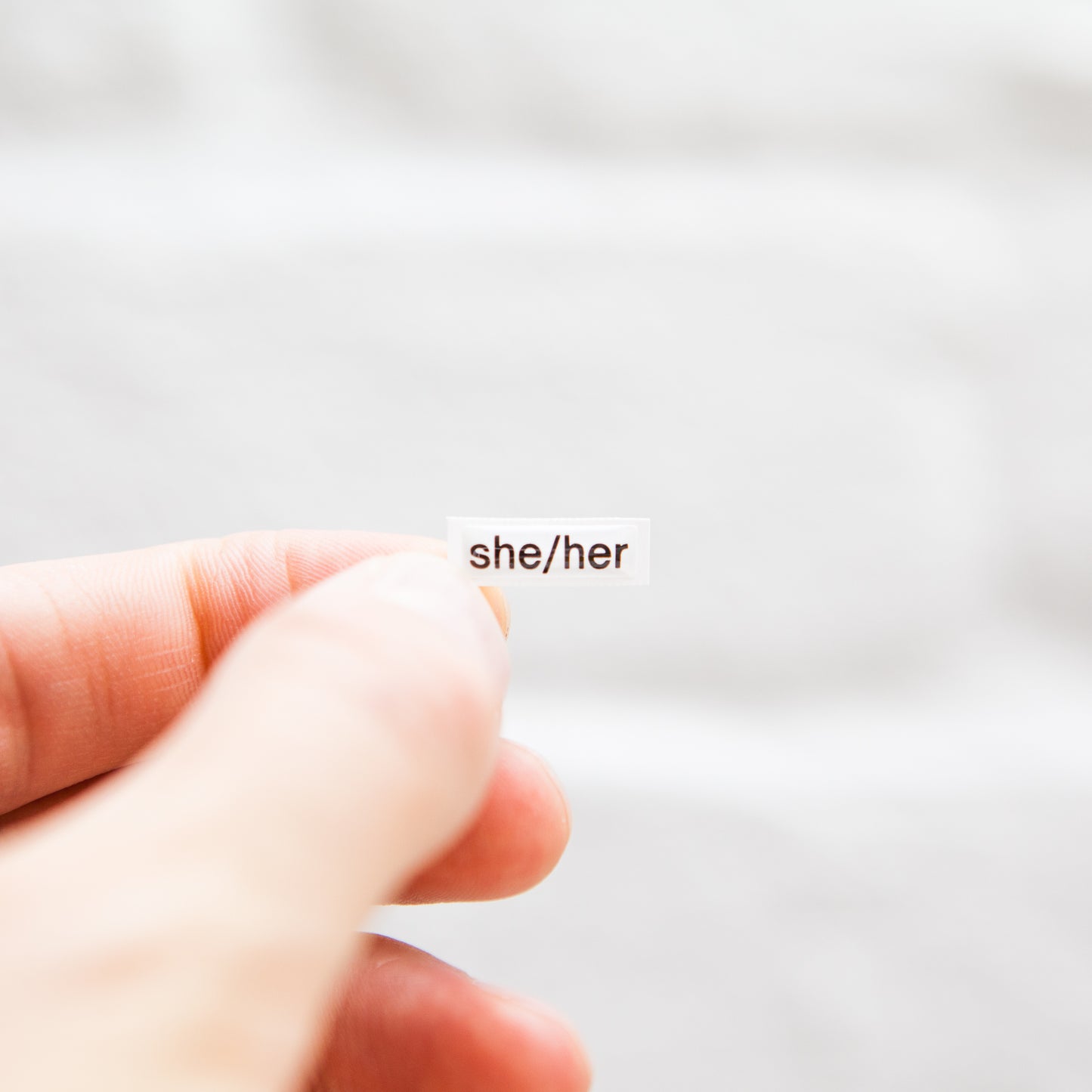 A white sticker with black text displaying she/her pronouns, designed for name badges and ID tags. A high-quality pronoun sticker with durable epoxy resin. This pronouns sticker for name badges