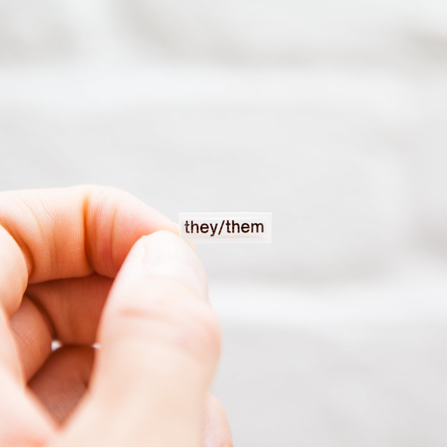 A white sticker with black text displaying they/them pronouns, designed for name badges and ID tags. A high-quality pronoun sticker with durable epoxy resin. This pronouns sticker for name badges