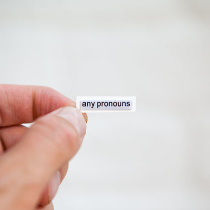 A white sticker with black text displaying 'any pronouns', designed for name badges and ID tags. A high-quality pronoun sticker with durable epoxy resin. This pronouns sticker for name badges